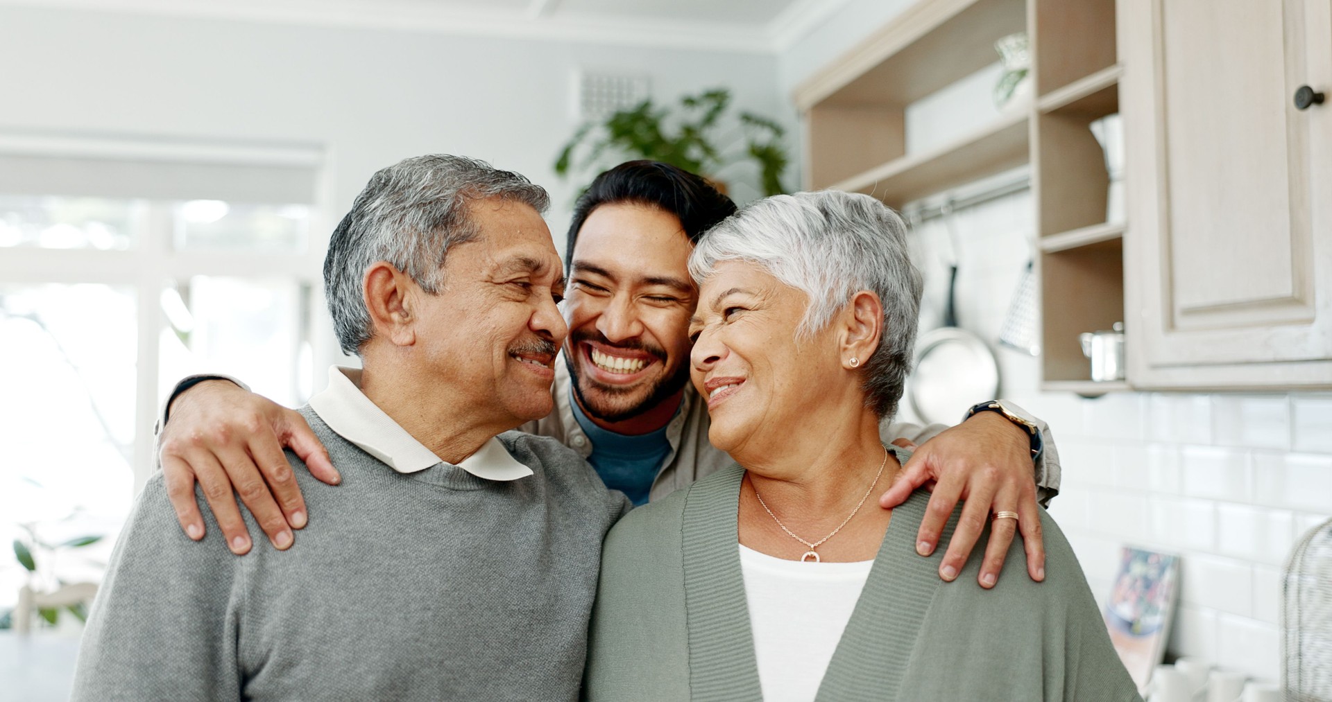 House, adult son and hug parents with weekend visit, welcome or bonding moment with smile, love or care. Happy family, senior people and embrace man in home for hello, comfort or affection in kitchen