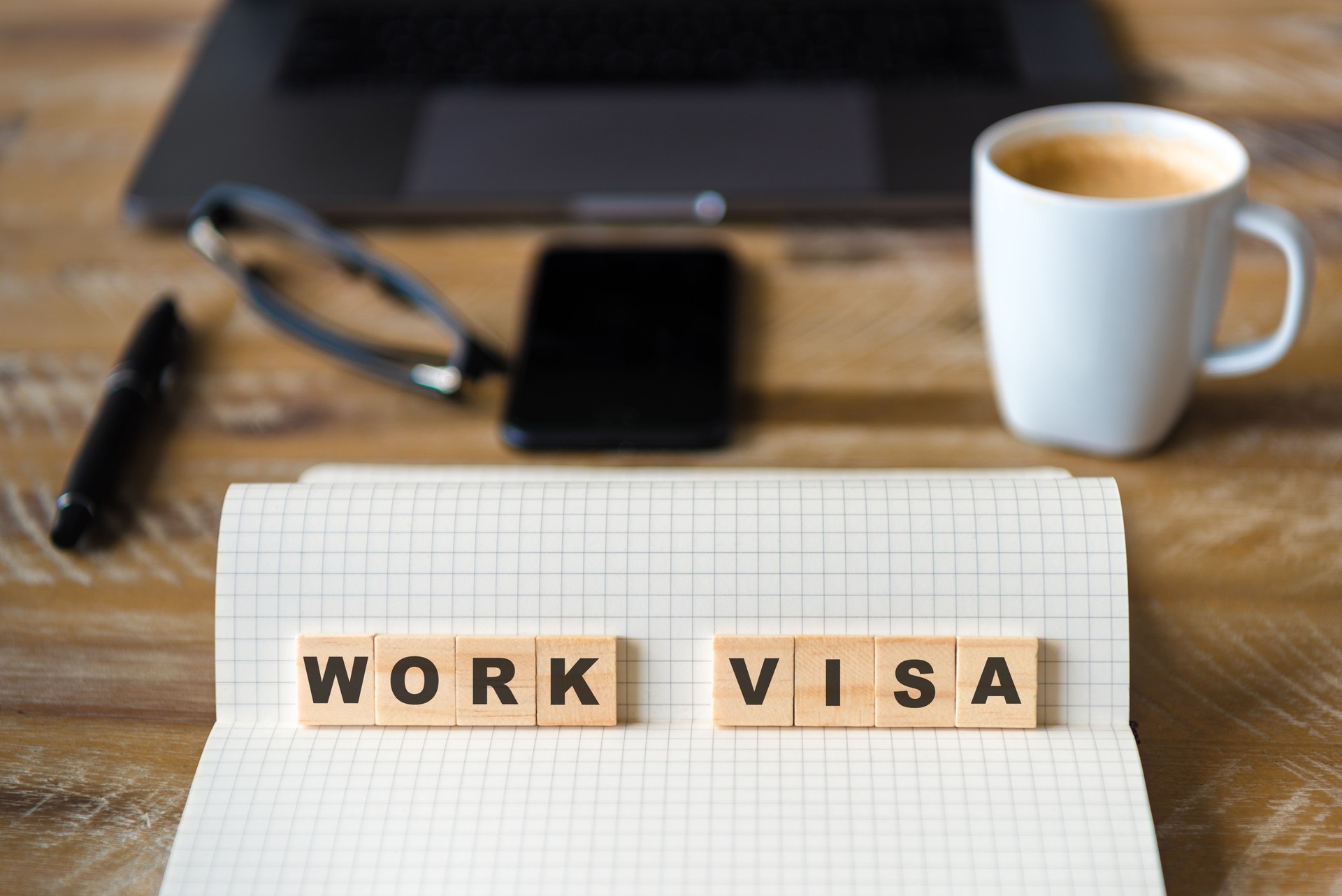 Closeup on notebook over wood table background, focus on wooden blocks with letters making Work Visa text